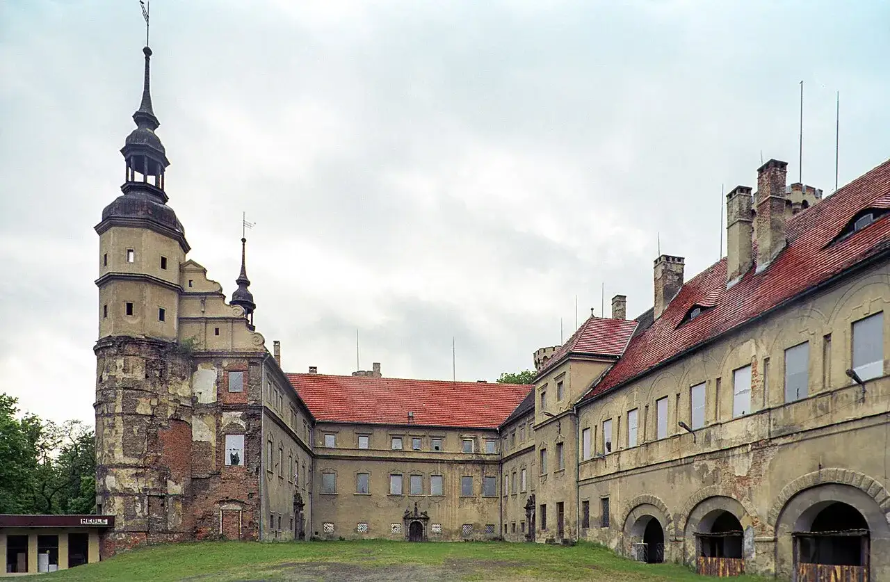 Zamek w Głog&oacute;wku, z charakterystyczną wieżą i czerwonymi dachami, prezentuje się majestatycznie na tle pochmurnego nieba.