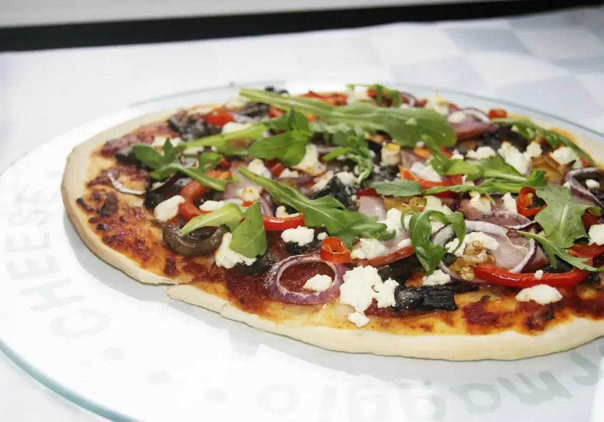 Pyszna pizza z serem feta, rukolą, papryką i cebulą na cienkim cieście.