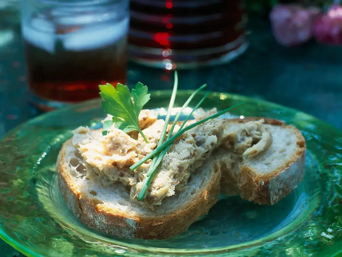 Tranches de pain de campagne garnies de rillettes de jambon, décorées de persil et de ciboule, sur une assiette verte.