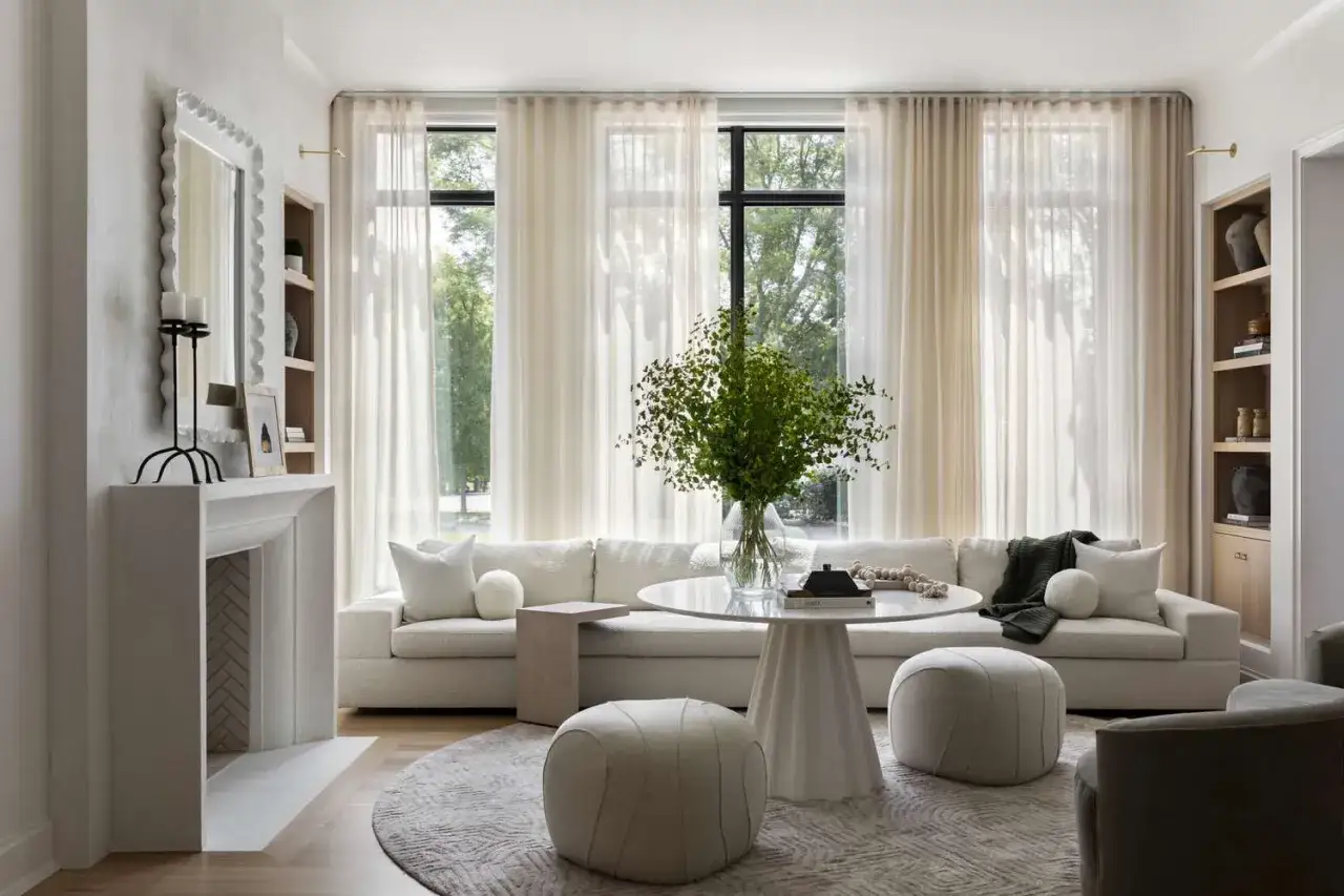 A serene living room with a plush sofa, round coffee table, and fireplace, embodying how to live a simple life with natural light and calming decor.
