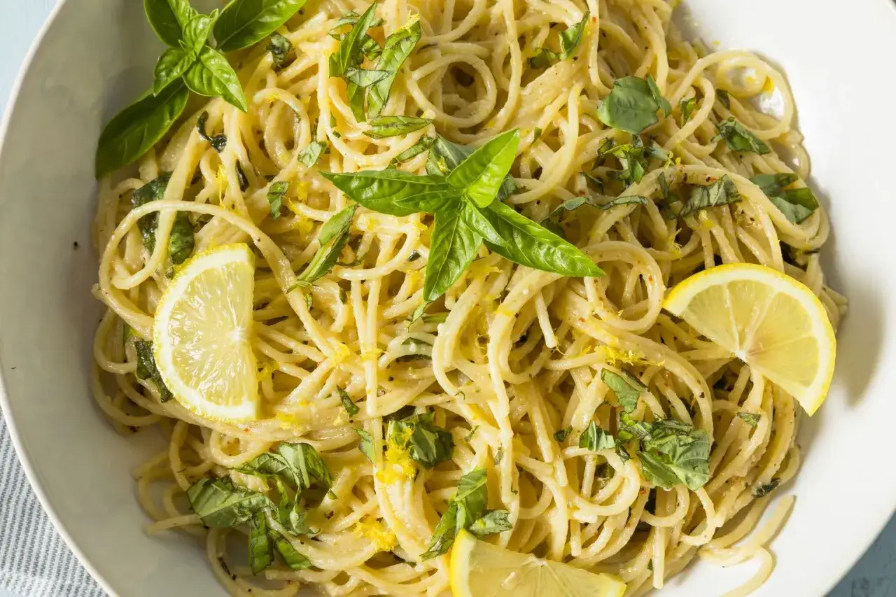 Pyszne spaghetti al limone z bazylią i plasterkami cytryny, posypane skórką cytrynową.