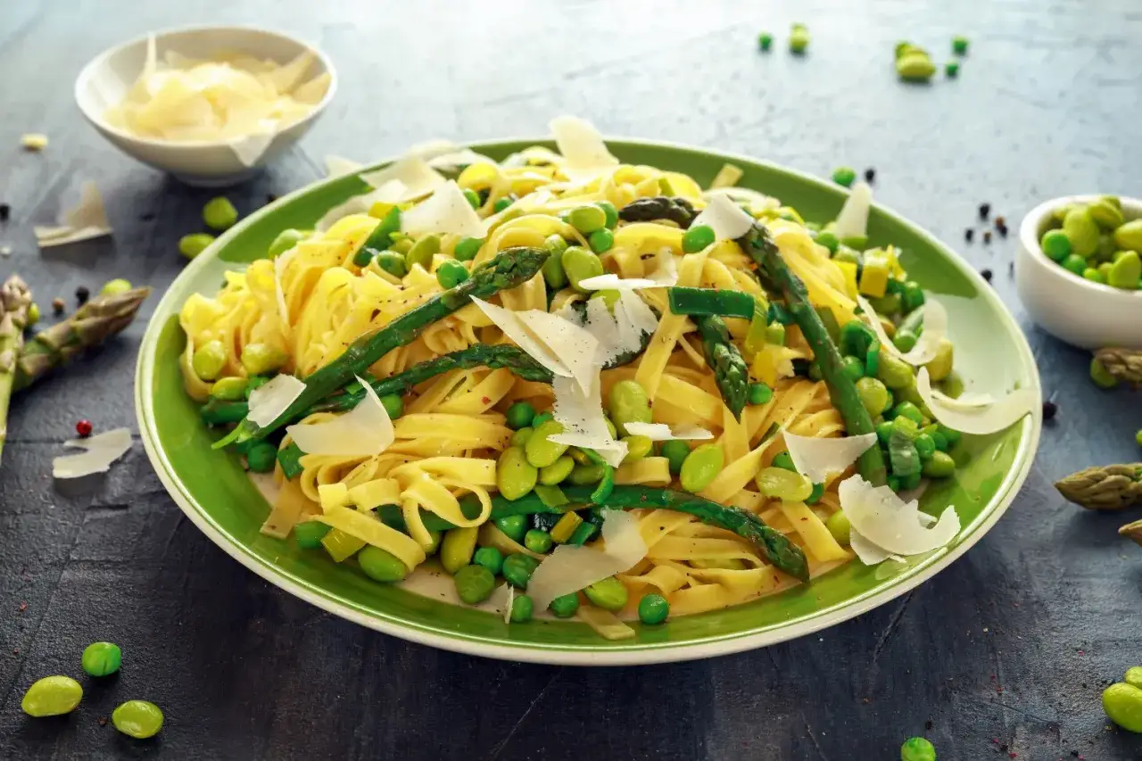 Un piatto di pasta con verdure fresche: tagliatelle condite con piselli, fave e asparagi, guarnite con scaglie di parmigiano.