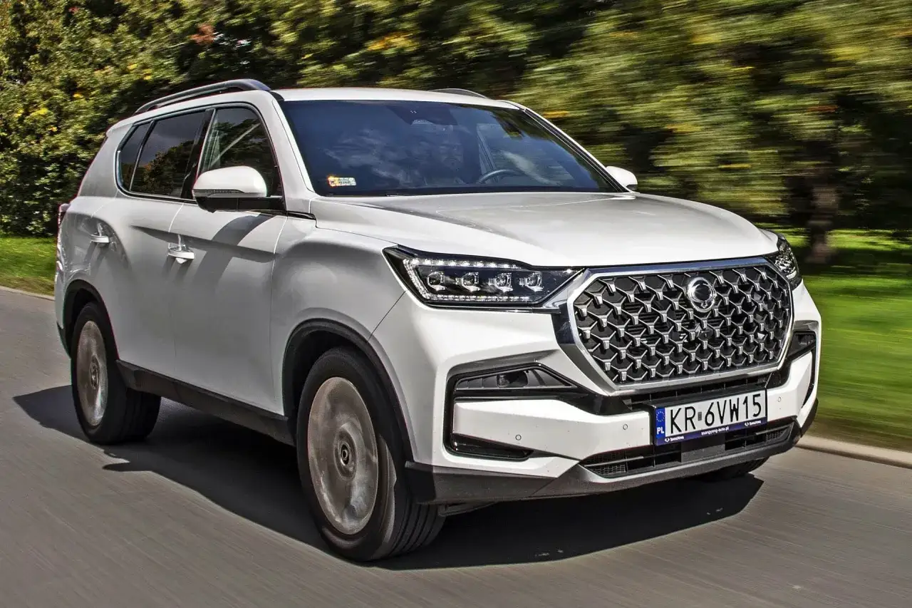 Biały SUV, jeden z koreańskich samochodów, pędzi po drodze wśród zieleni.
