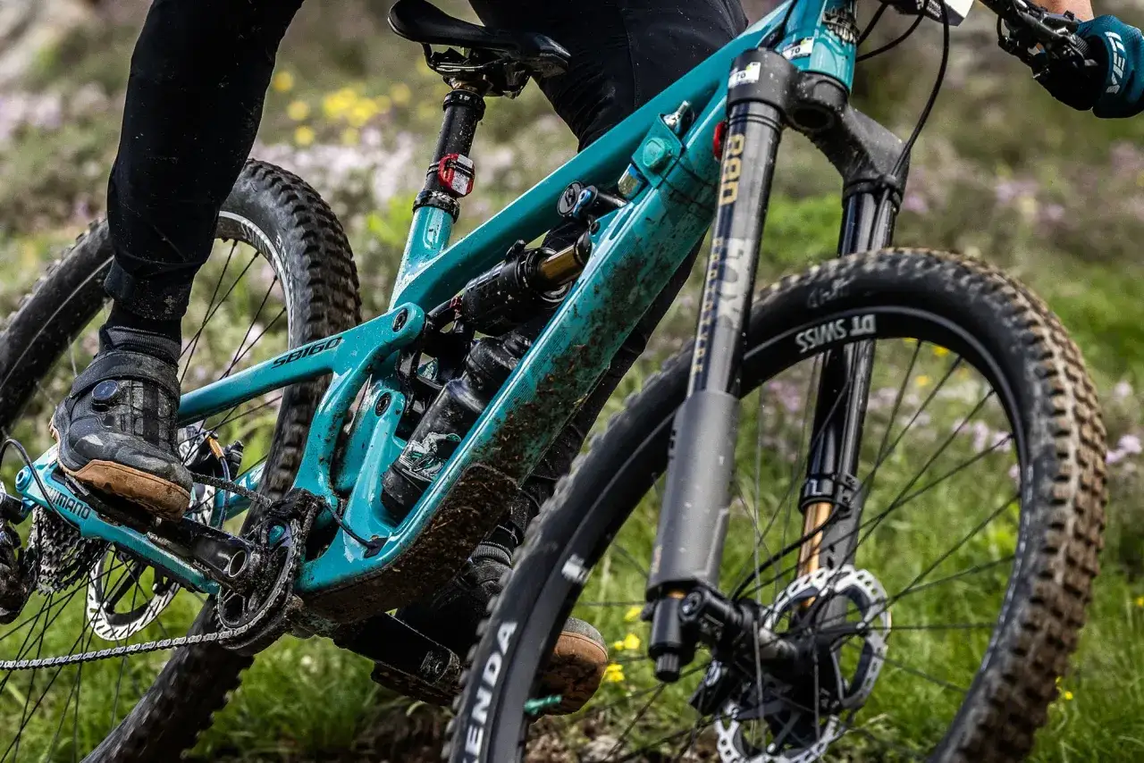 A rider's foot on a pedal of a teal single fork mountain bike, ready to tackle a trail.