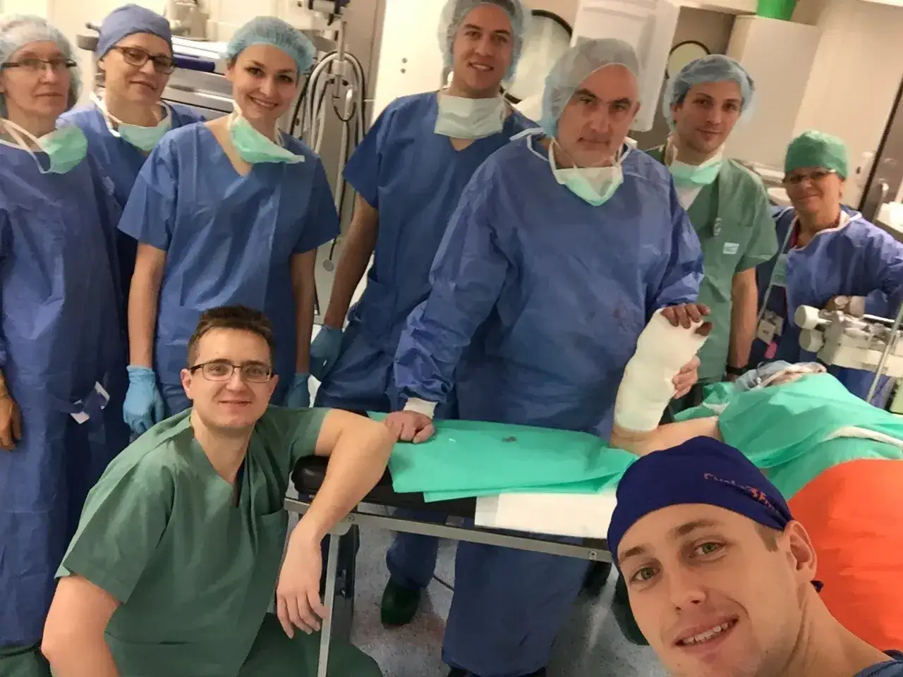 Zespół medyczny w strojach operacyjnych pozuje do zdjęcia w sali operacyjnej, jeden z lekarzy trzyma nogę w gipsie.