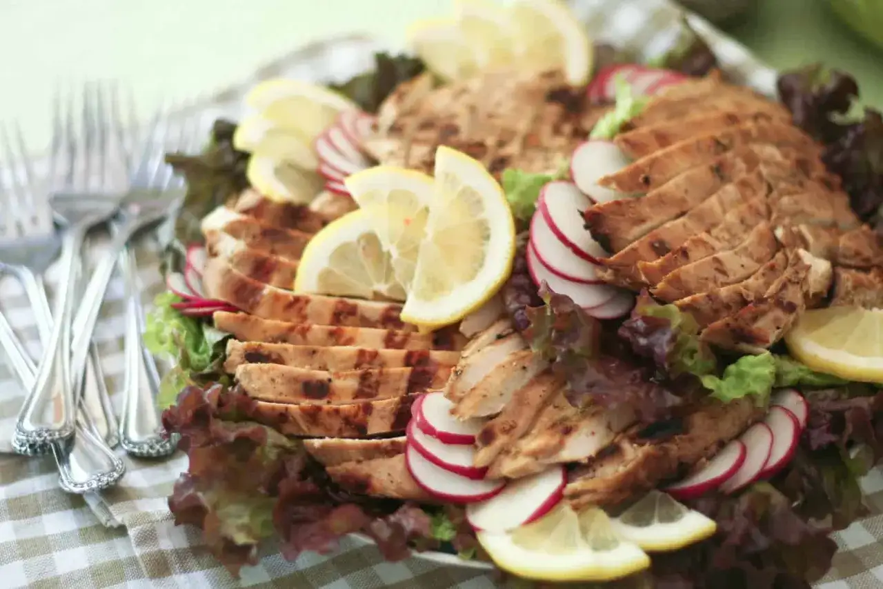 En tallrik med dubbelmarinerad kyckling, skivad och serverad med sallad, r&auml;disor och citronklyftor. Vackert upplagd f&ouml;r en h&auml;rlig m&aring;ltid.