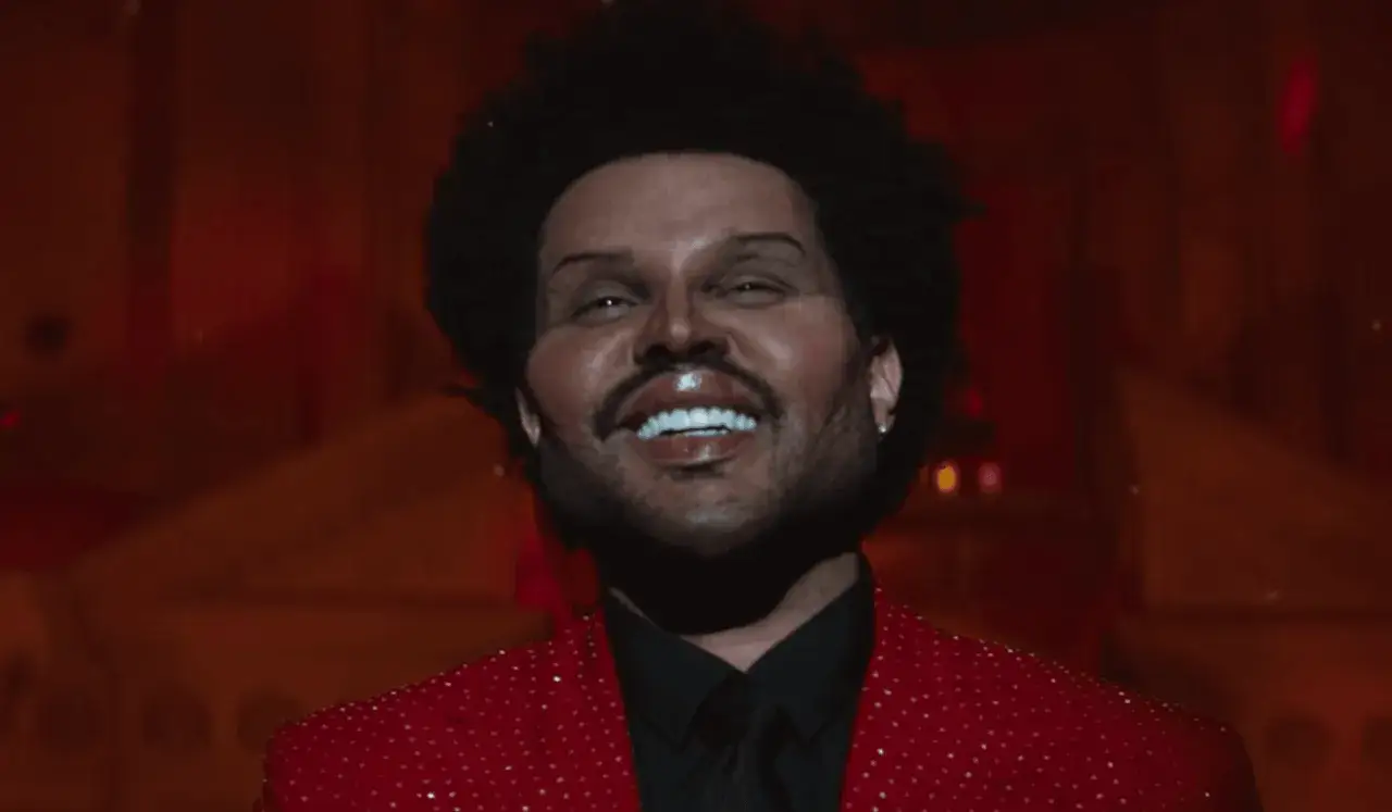 The Weeknd w czerwonej, błyszczącej marynarce, z charakterystyczną fryzurą i makijażem, jak z jego filmów.