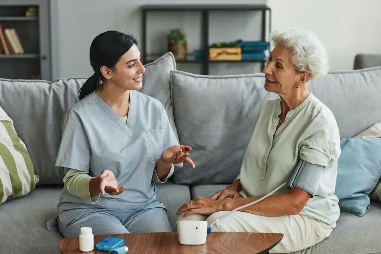 Pflegekraft misst Blutdruck bei &auml;lterer Dame. Sie spricht ermutigend, um ihr zu helfen, **raus aus der sozialen Arbeit** und zur&uuml;ck ins Leben zu finden.