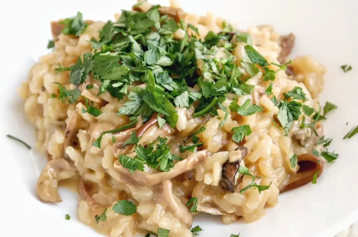 Kremowe risotto z grzybami, posypane świeżą natką pietruszki. Idealne danie dla miłośników leśnych smaków.
