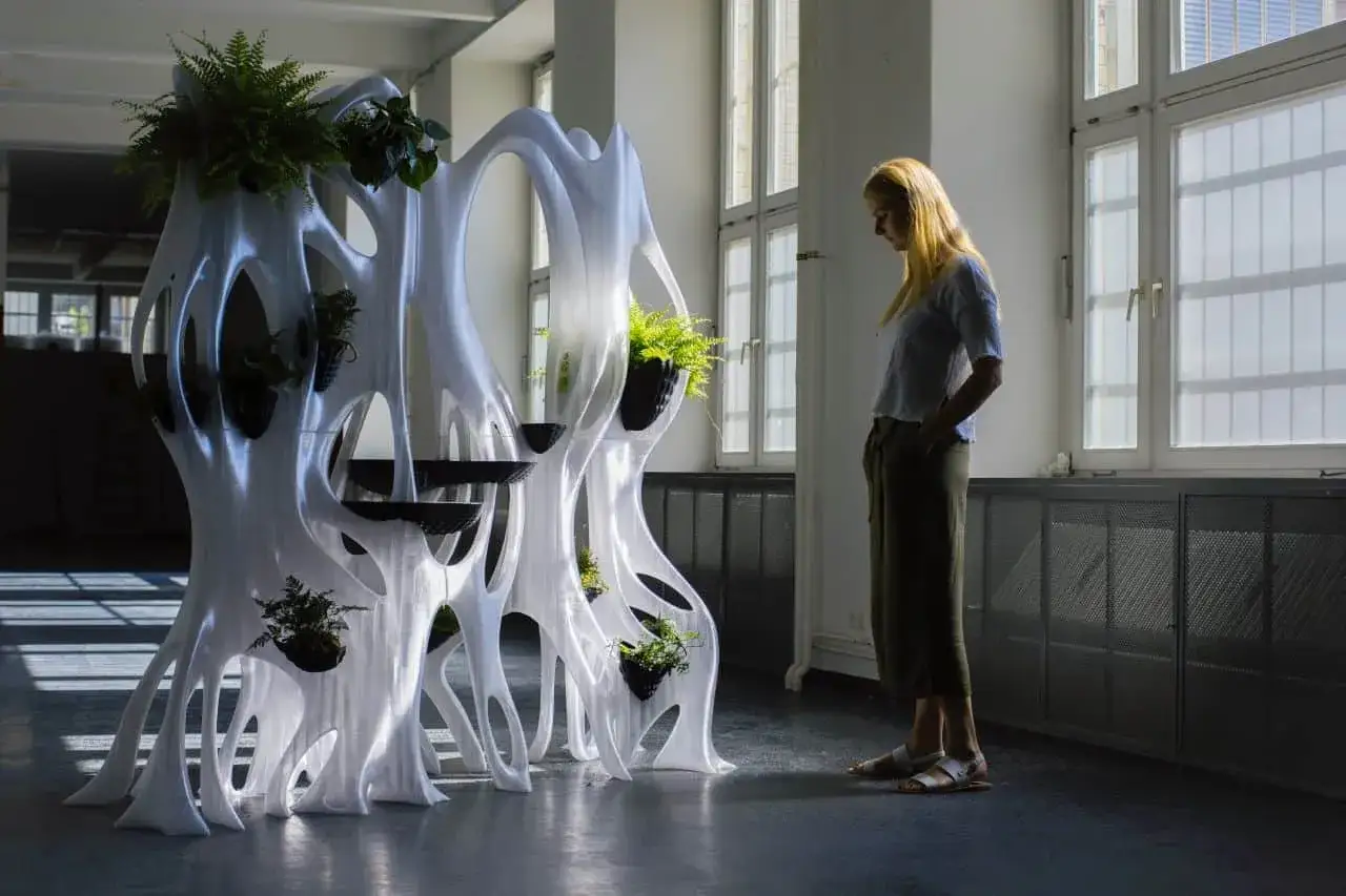 A woman admires a white, organic structure, a testament to generative design software, filled with lush plants.