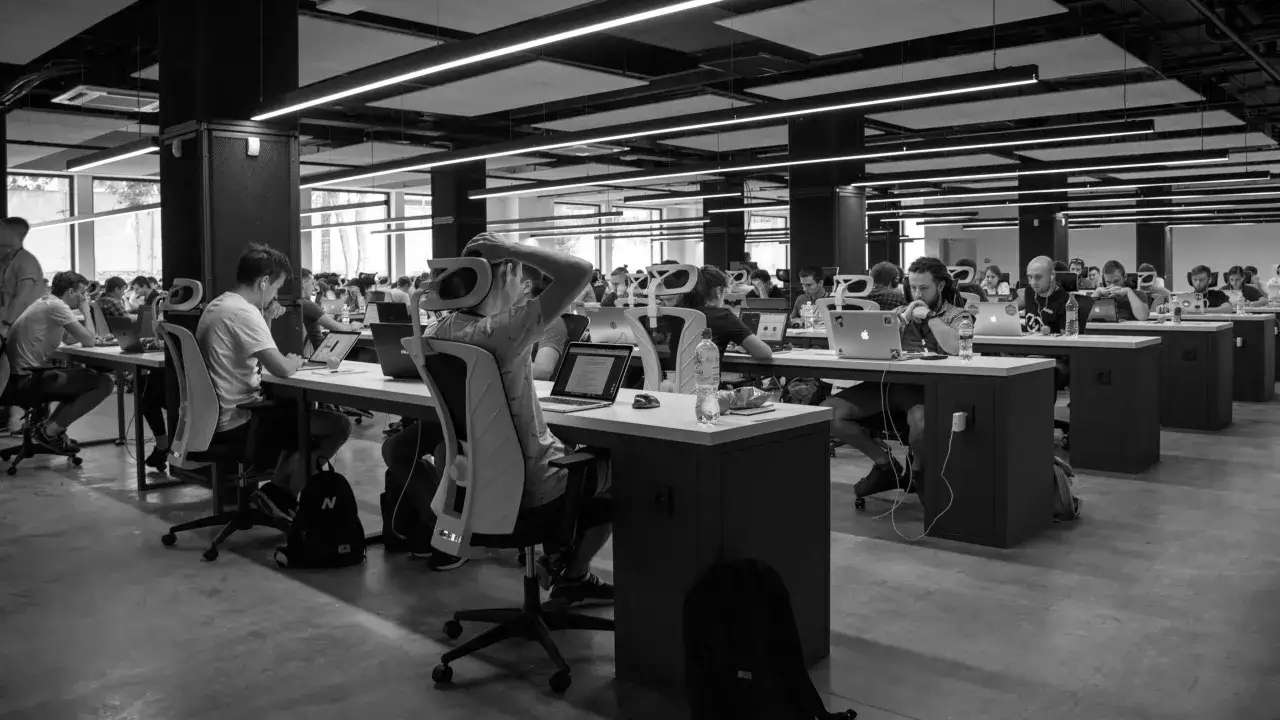 Otwarta przestrzeń biurowa z pracującymi ludźmi przy biurkach z laptopami.