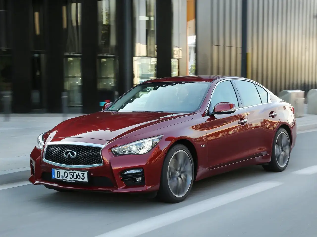 Czerwony infiniti samochód w ruchu miejskim, z nowoczesną architekturą w tle.