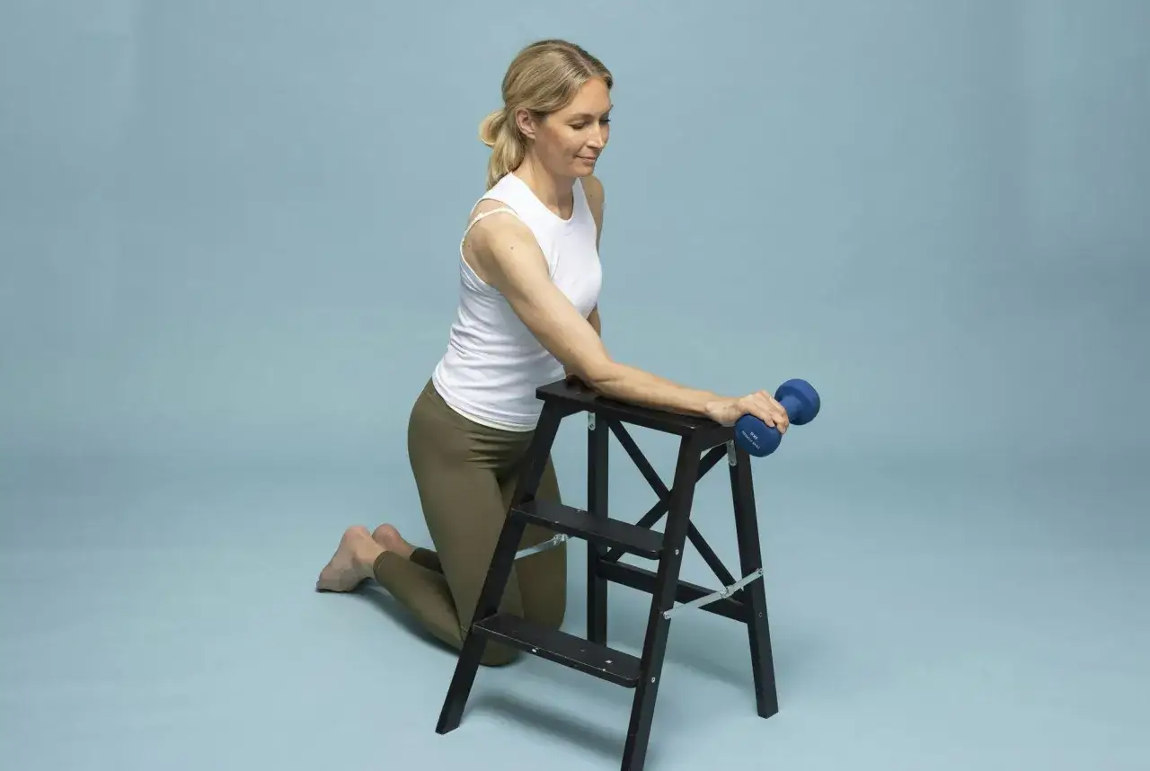 Kvinna med tennisarmbåge utför rehabiliteringsträning med hantel på en pall.
