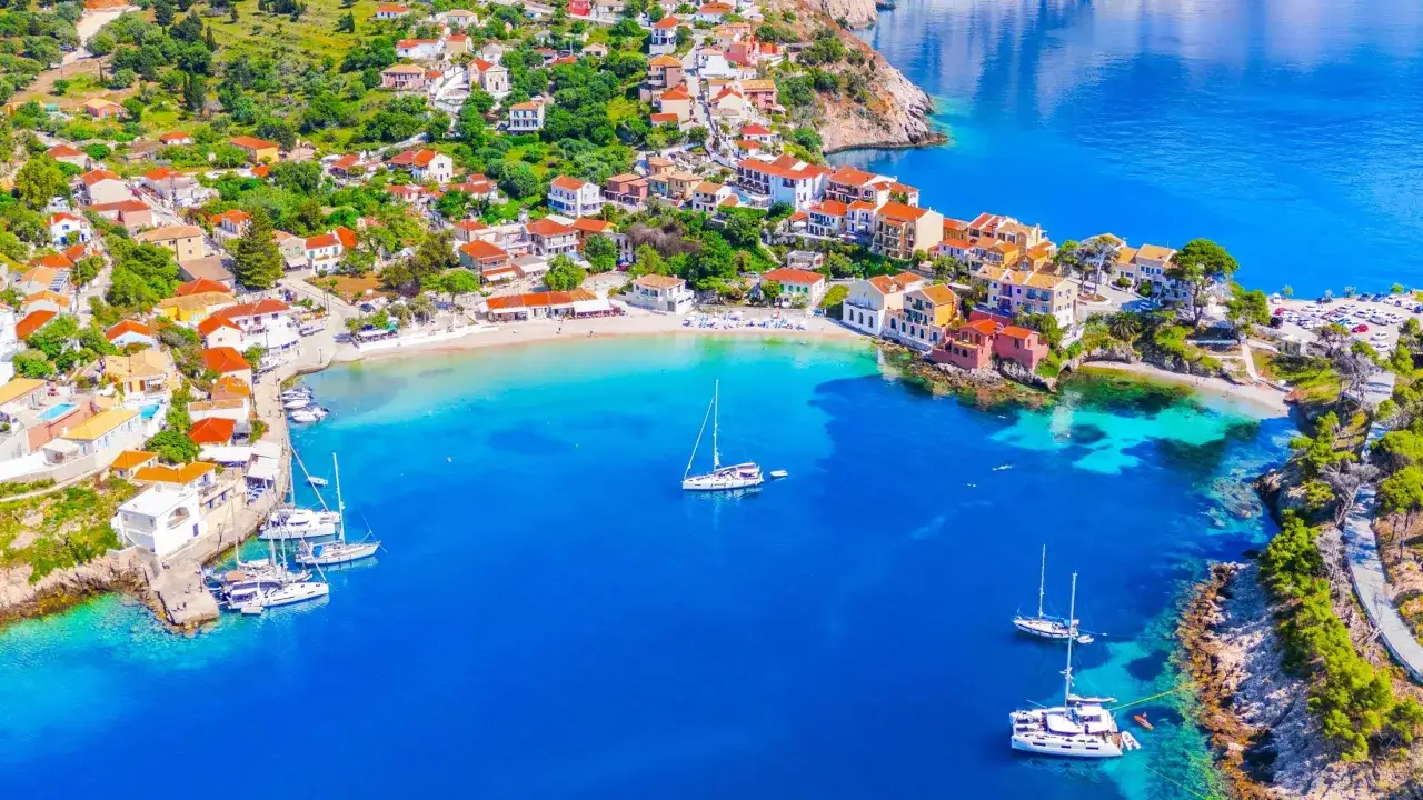 Traumhafter **Kefalonia Strand** mit bunten Häusern, türkisfarbenem Wasser und Segelbooten.