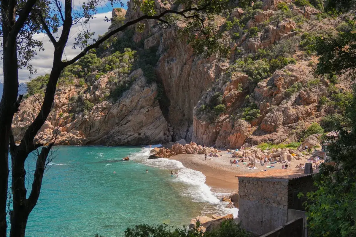 Malownicza zatoczka z turkusową wodą i skalistymi zboczami. Czy to Sardynia, czy Korsyka? Ludzie odpoczywają na plaży.