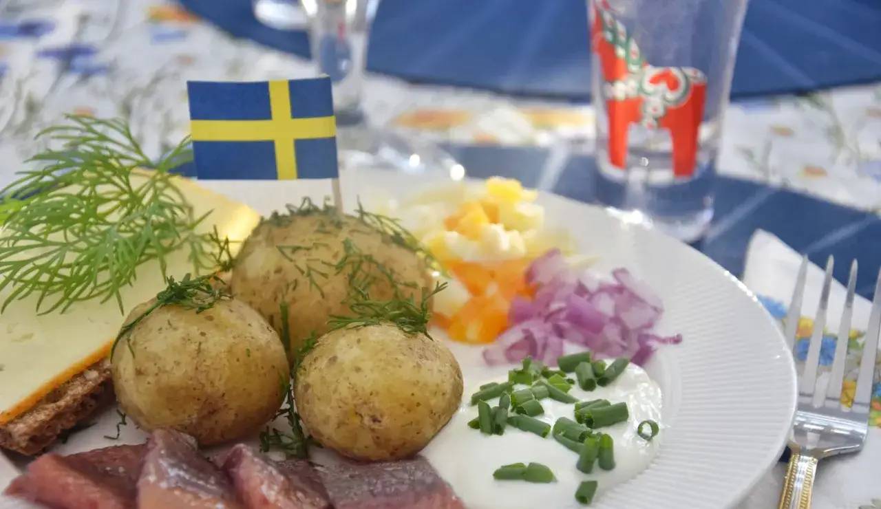 En tallrik med sill, färskpotatis, ost och dill. En svensk flagga vajar stolt. Perfekt mat midsommar!