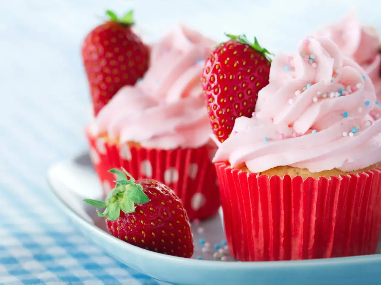 Erdbeer Cupcakes mit rosa Zuckerguss und frischen Erdbeeren, verziert mit bunten Streuseln.