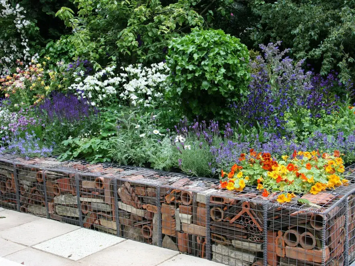 Kreative **Ideen Gartenmauer**: Gabionen gef&uuml;llt mit Ziegeln und Rohren, bepflanzt mit bunten Blumen und Lavendel.