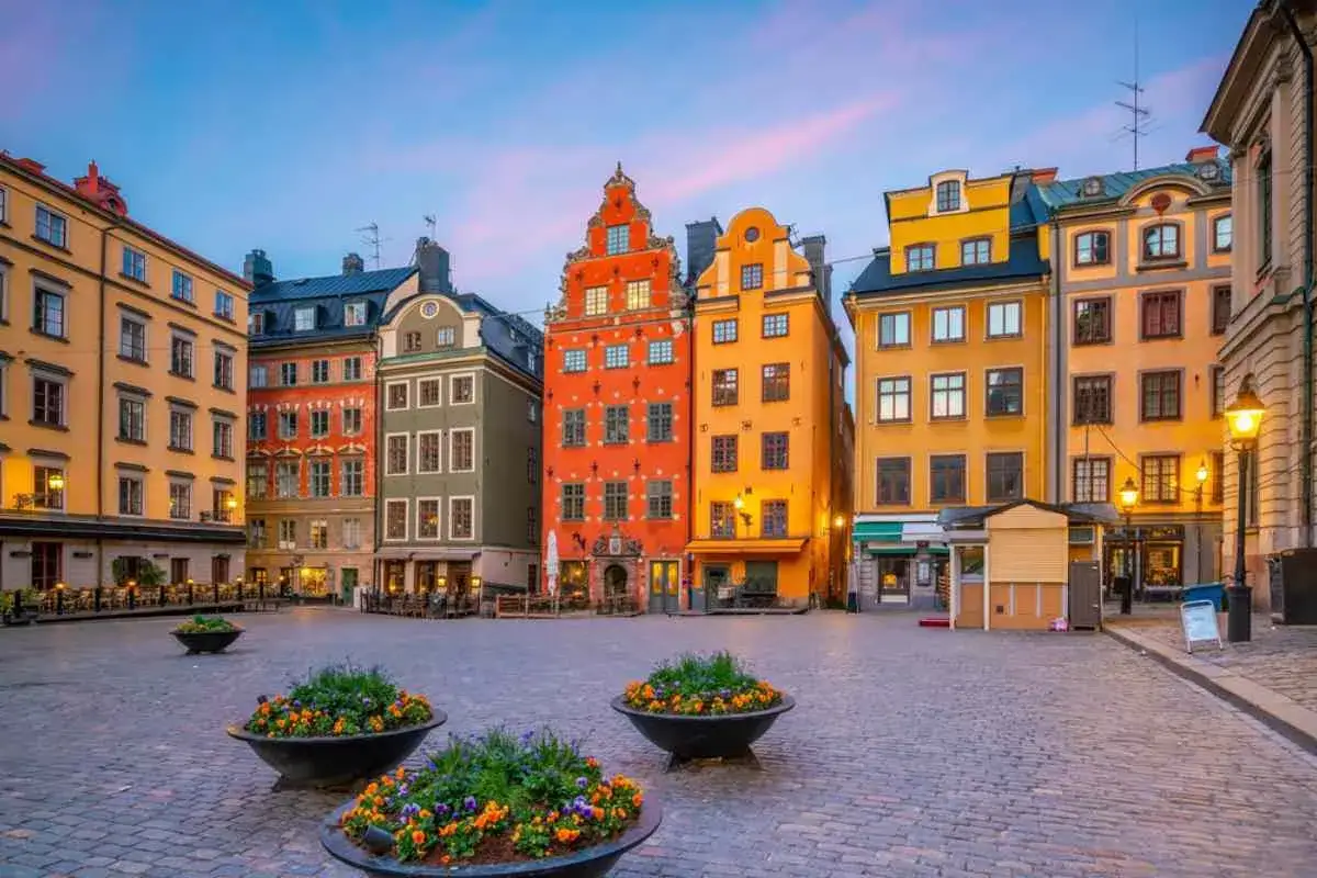 Färgstarka hus i Gamla stan, Stockholm, med kullerstensbelagd torg och blomsterurnor.