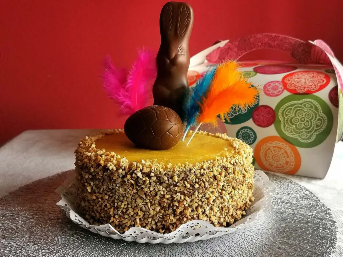 Deliciosa receta mona de pascua esponjosa, decorada con un conejito de chocolate, huevo y plumas de colores.