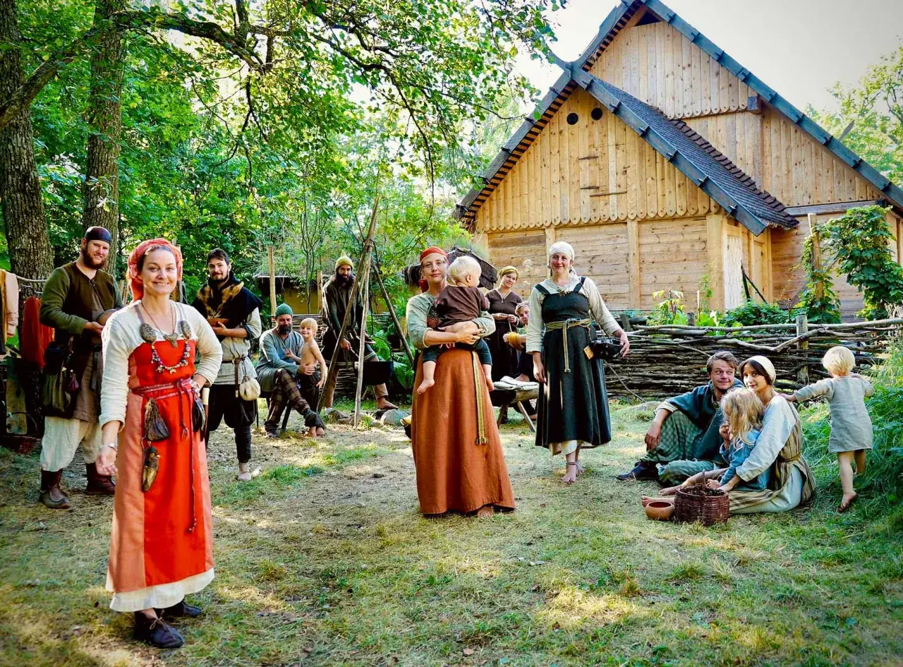 En grupp människor i vikingakläder samlas framför ett trädhus i vikingabyn Storholmen.