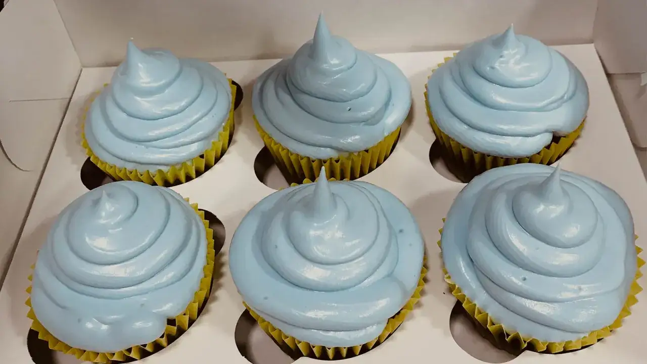 Seis cupcakes con glaseado de merengue italiano azul pálido, en sus envoltorios amarillos, listos para ser disfrutados.