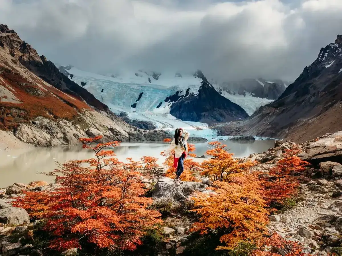 Frau genie&szlig;t Herbstfarben in Patagonien. Die beste Reisezeit f&uuml;r dieses Naturschauspiel ist der Herbst, mit leuchtendem Orange und Rot vor einem Gletscher.