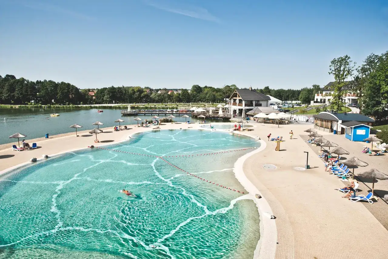 Słoneczny dzień nad jeziorem, ludzie odpoczywają przy basenie i plaży. Sprawdź molo Osiek cennik, by zaplanować swój pobyt.