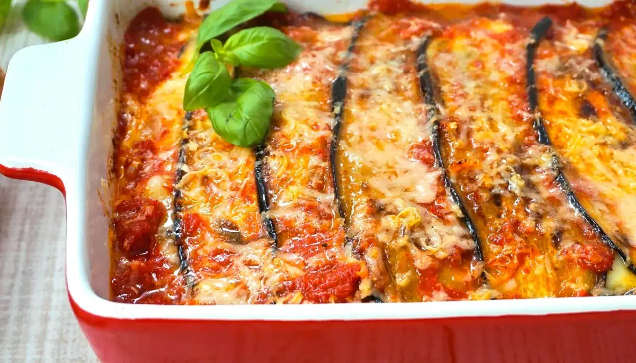 Berenjenas a la parmesana recién horneadas, burbujeantes y doradas, con queso fundido y hojas de albahaca fresca.