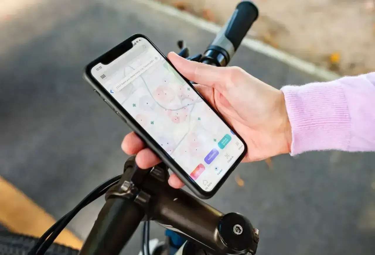Dłoń trzyma smartfon z mapą i ikonami. To aplikacja na rower, która pomaga w nawigacji i monitorowaniu trasy.
