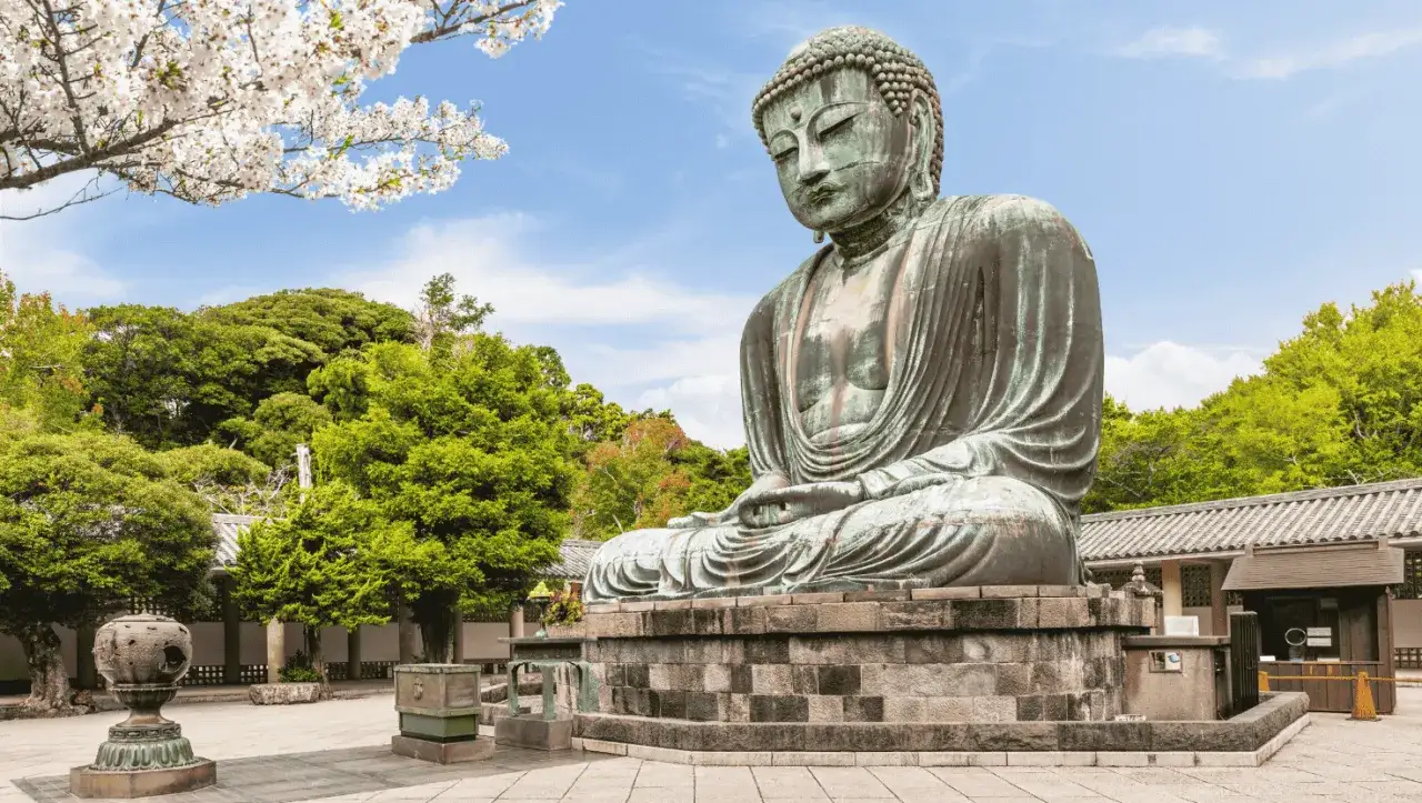 El Gran Buda de bronce, una maravilla que ver en Kamakura, sentado serenamente bajo cerezos en flor y rodeado de exuberante vegetación.