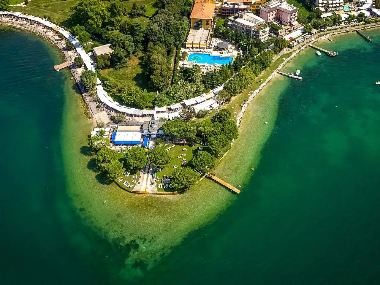 Ein idyllischer Gardasee Strand mit t&uuml;rkisfarbenem Wasser, Liegest&uuml;hlen und B&auml;umen.