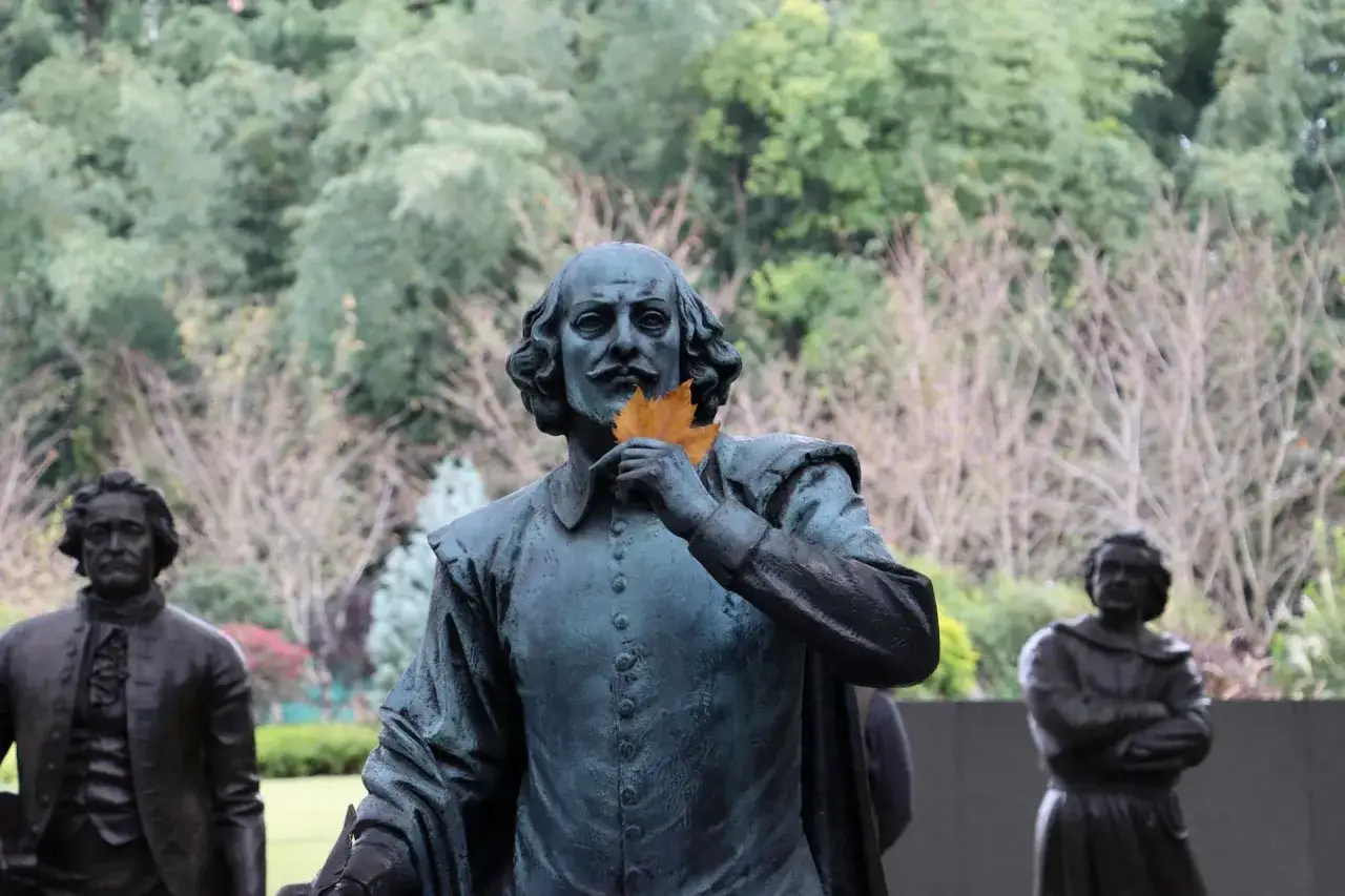 Staty av Shakespeare med ett löv framför munnen, som ett sonett exempel. Bakom syns fler statyer och träd.