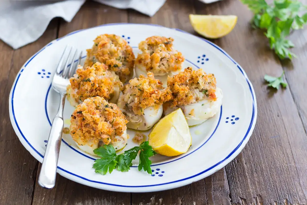 Seppie al forno ripiene, dorate e croccanti, servite su un piatto bianco con limone e prezzemolo.