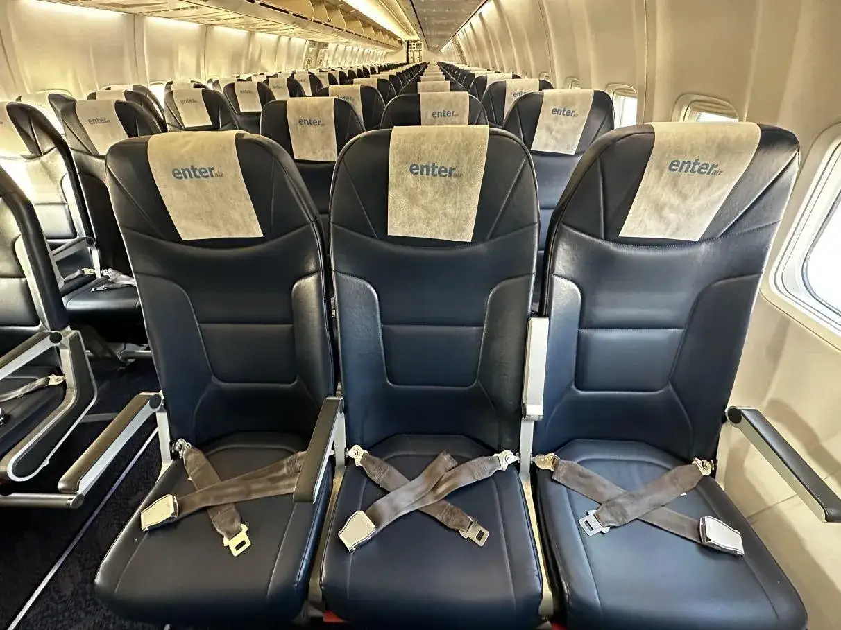 Puste fotele w samolocie Enter Air. Wnętrze kabiny z rzędami ciemnych siedzeń i zagłówkami z logo przewoźnika.