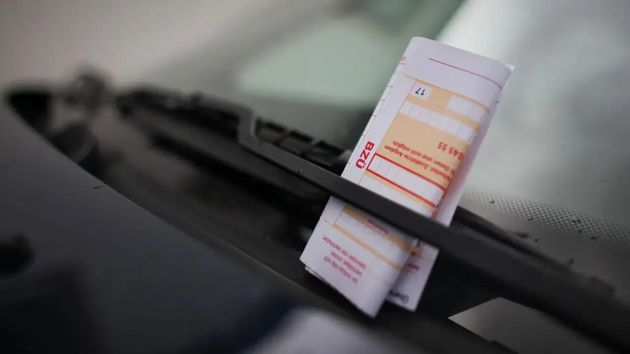 Ein Strafzettel am Auto wegen Parken. Der Zettel ist unter dem Scheibenwischer eingeklemmt.