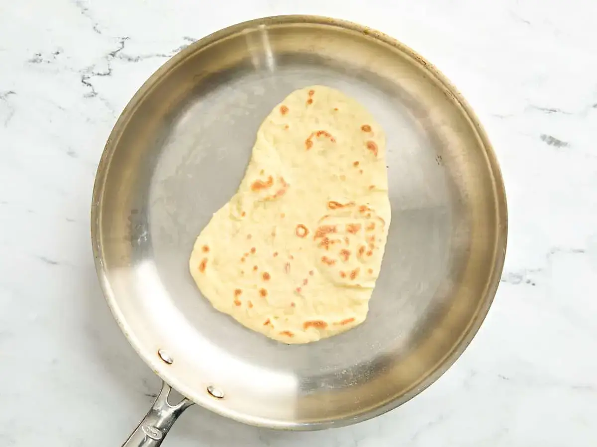 Ein Naan Brot br&auml;unt in einer Pfanne.