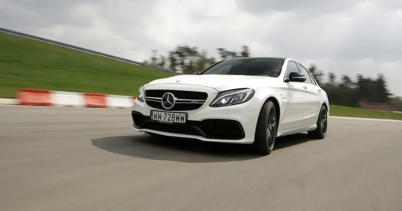 Biały Mercedes-AMG C63 Coupe pędzi po torze wyścigowym, zostawiając za sobą rozmyte tło.