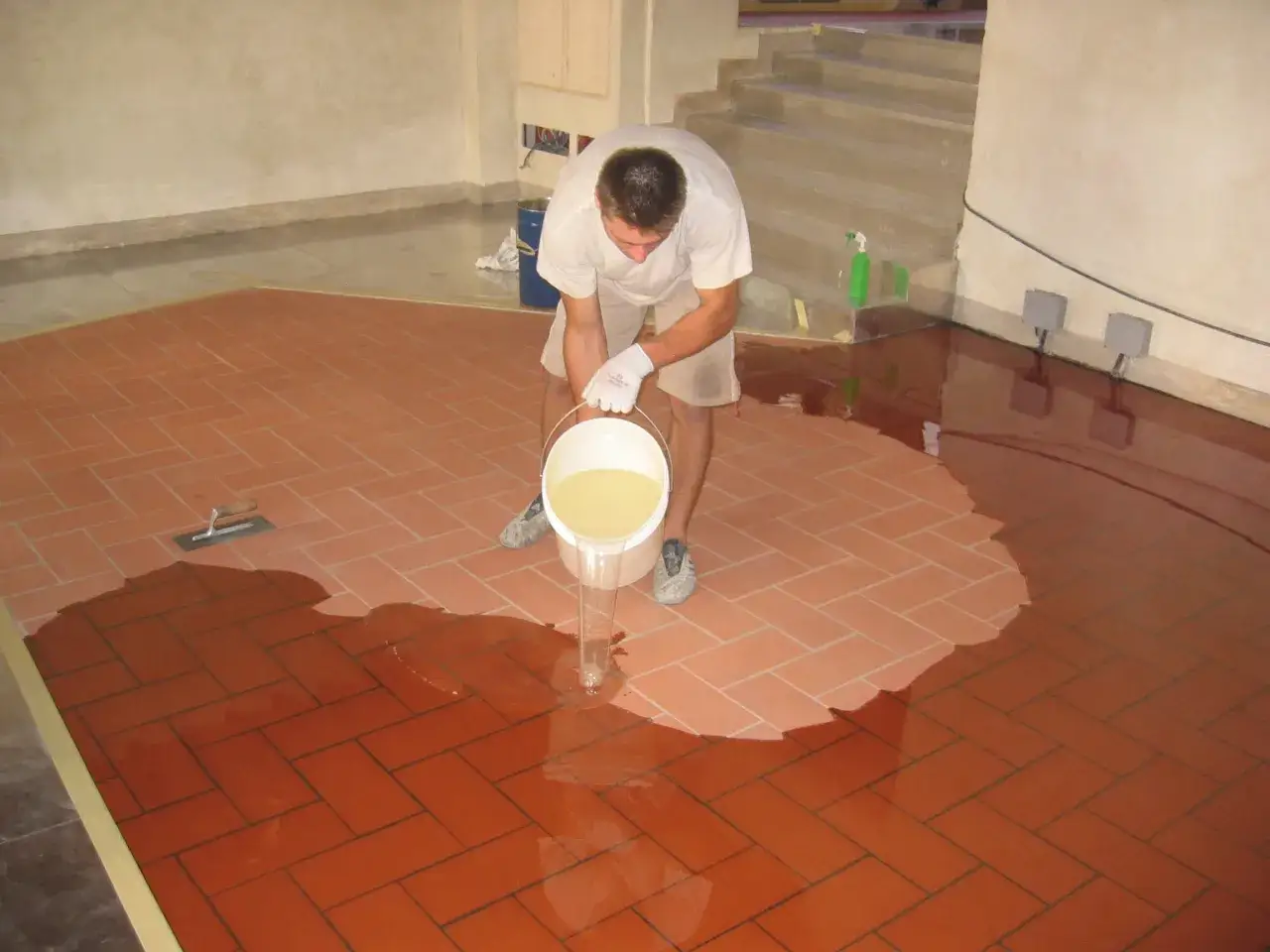 Operaio versa resina liquida su un pavimento in cotto, creando un nuovo pavimento in resina sopra piastrelle.