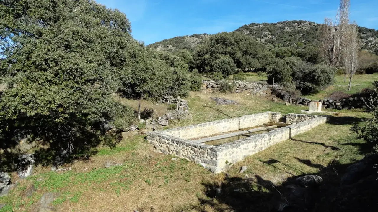 Lavadero de piedra en la serrada de la fuente, rodeado de vegetación y colinas.