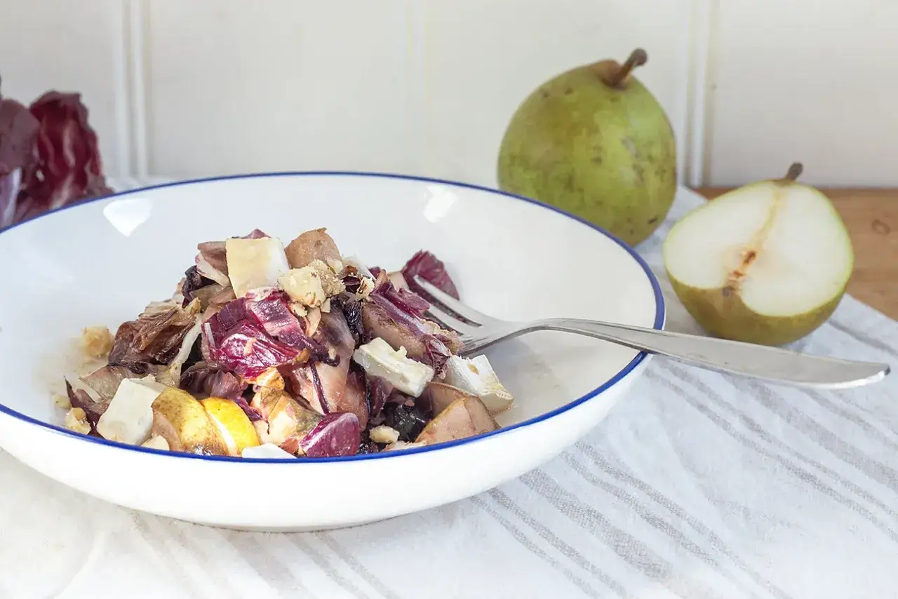 Ein köstlicher Radicchio Salat mit Birnenstücken und Nüssen, serviert in einer weißen Schüssel mit blauem Rand.