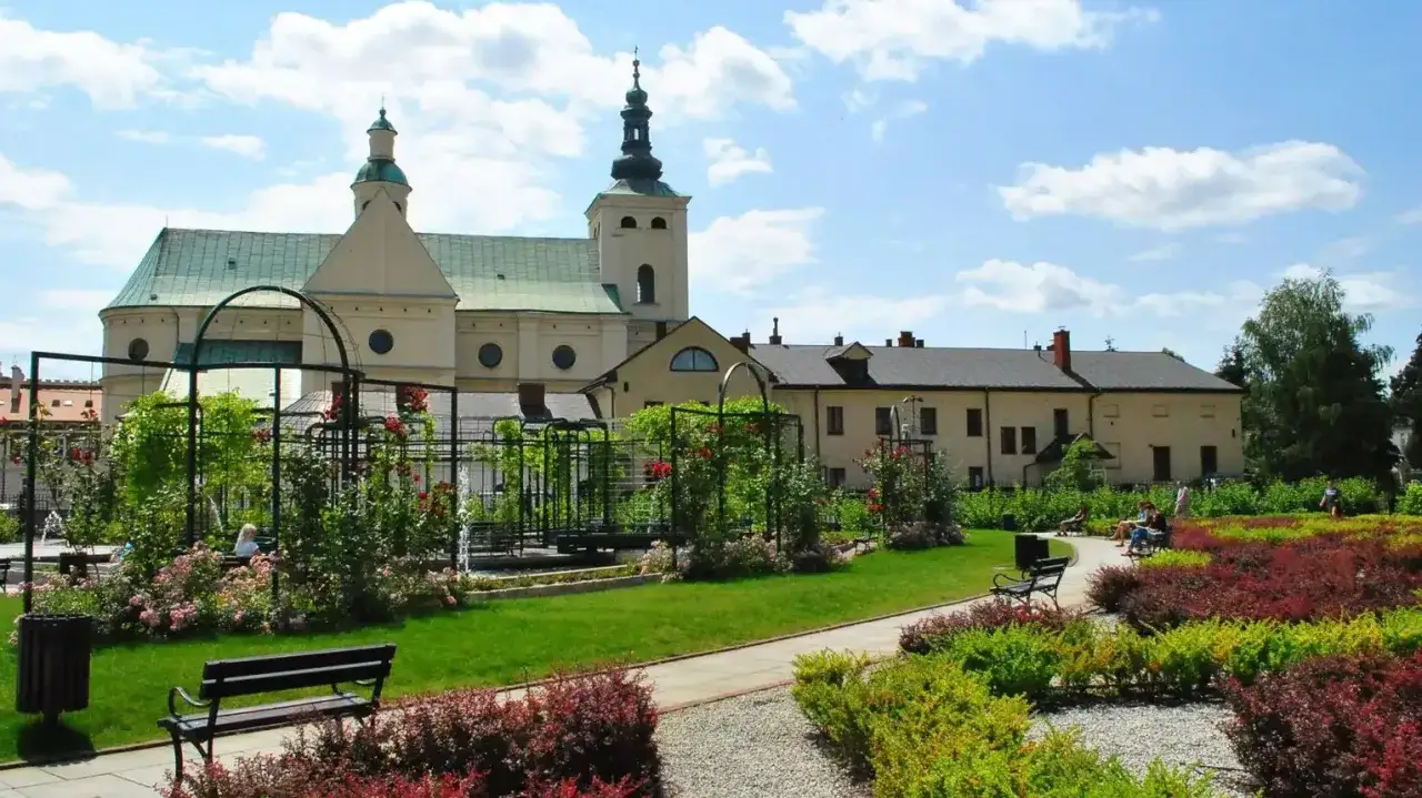 Piękne ogrody bernardyńskie Rzeszów z kwitnącymi różami i zabytkowym kościołem w tle.
