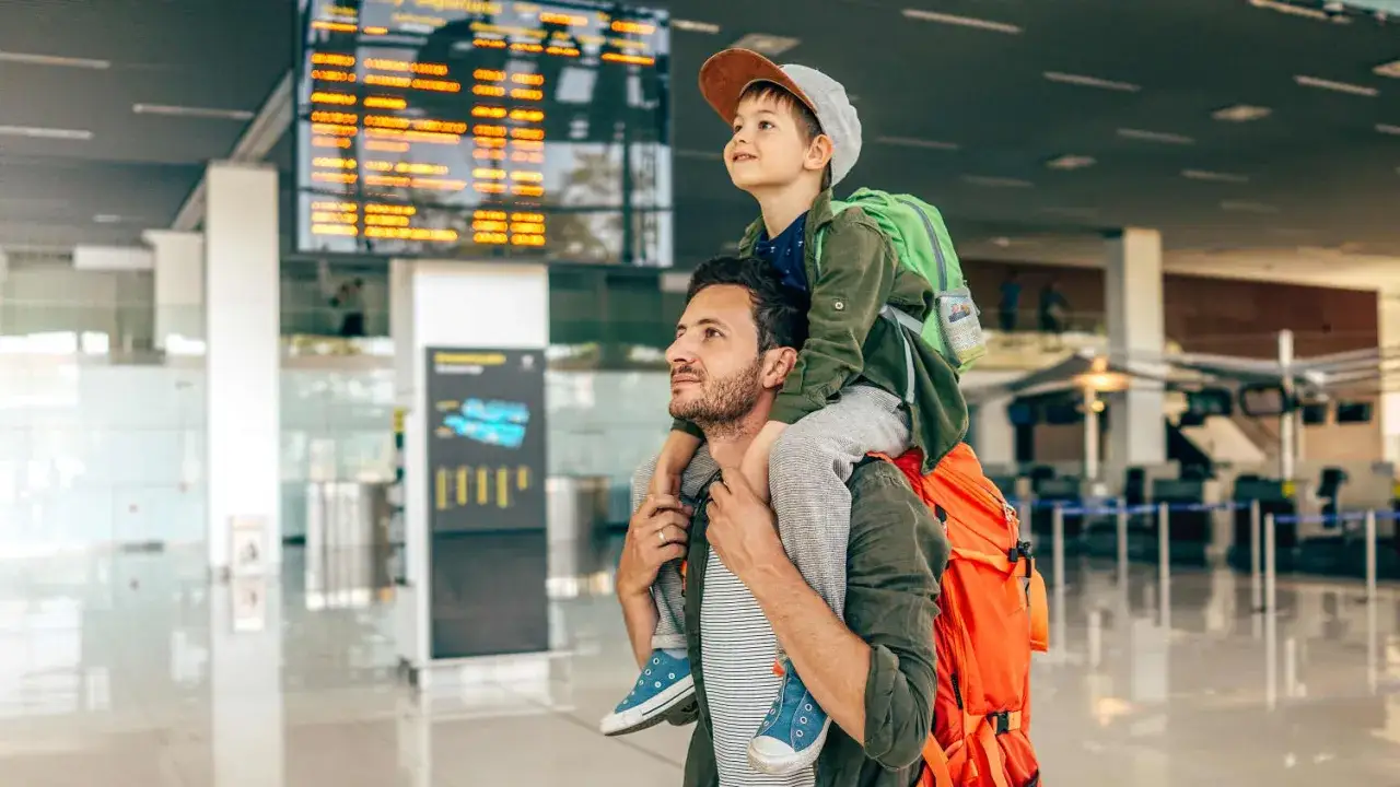 Vater trägt Sohn auf den Schultern am Flughafen. Ein Abenteuer beginnt, alleine reisen mit Kind.