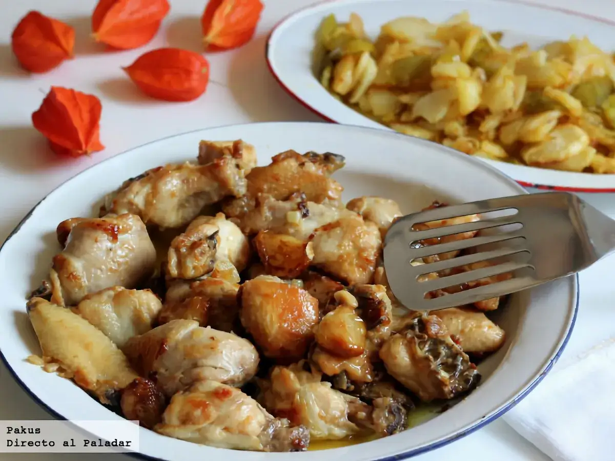 Sabroso pollo al ajillo servido en una fuente, con una esp&aacute;tula lista para servir. Al fondo, otro plato con patatas y pimientos.