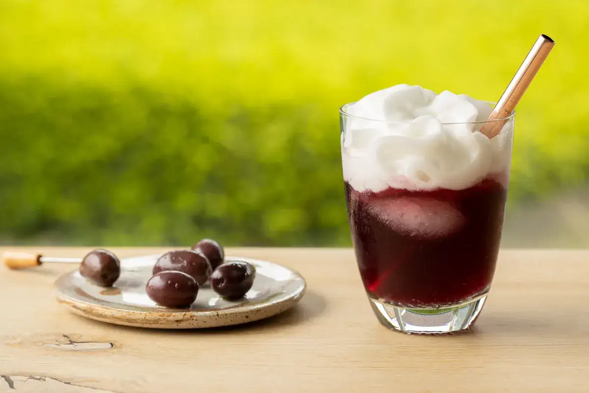 Refrescante tinto de verano con espuma de limón, acompañado de aceitunas en un plato.