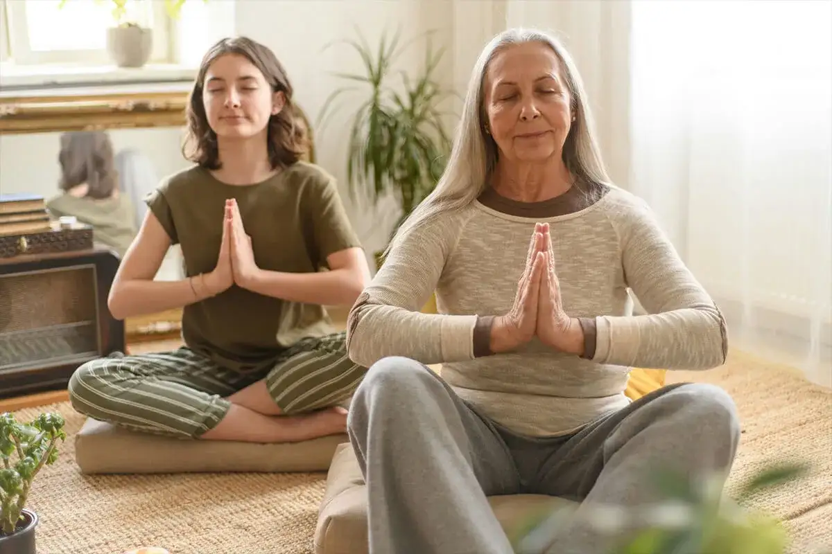 Une jeune fille et une femme plus âgée méditent ensemble. Une belle façon de gérer le stress et de savoir comment ne pas grossir à la ménopause.