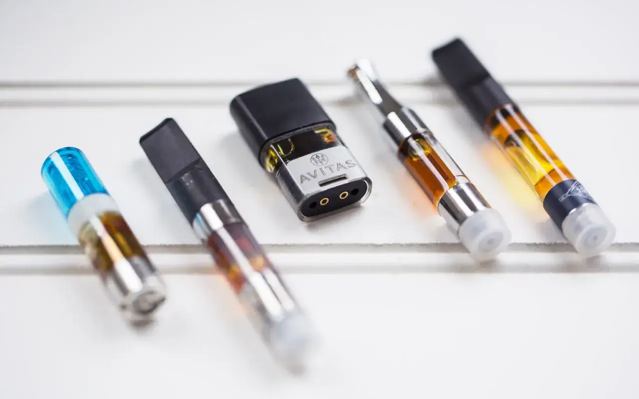 Varios cartuchos vaper de diferentes tamaños y colores, algunos con líquido ámbar y uno con tapa azul.