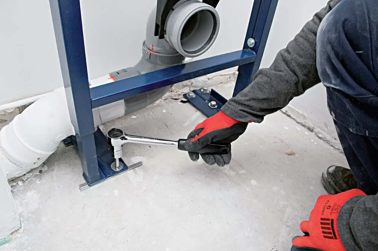 Main tenant utilise une clé pour fixer le bâti-support lors de l'installer wc suspendu.
