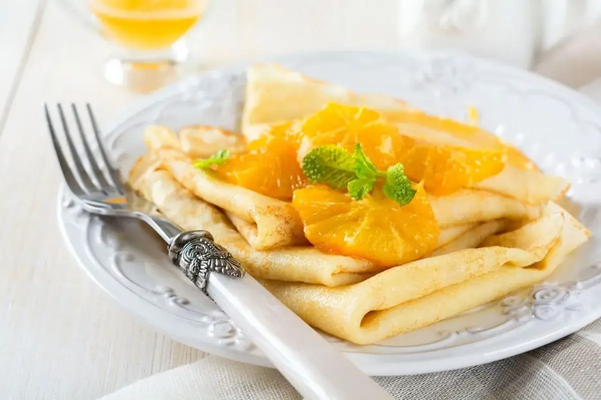 Deliziose crepes senza uova, guarnite con spicchi d'arancia succosa e foglioline di menta fresca. Un dolce leggero e profumato.