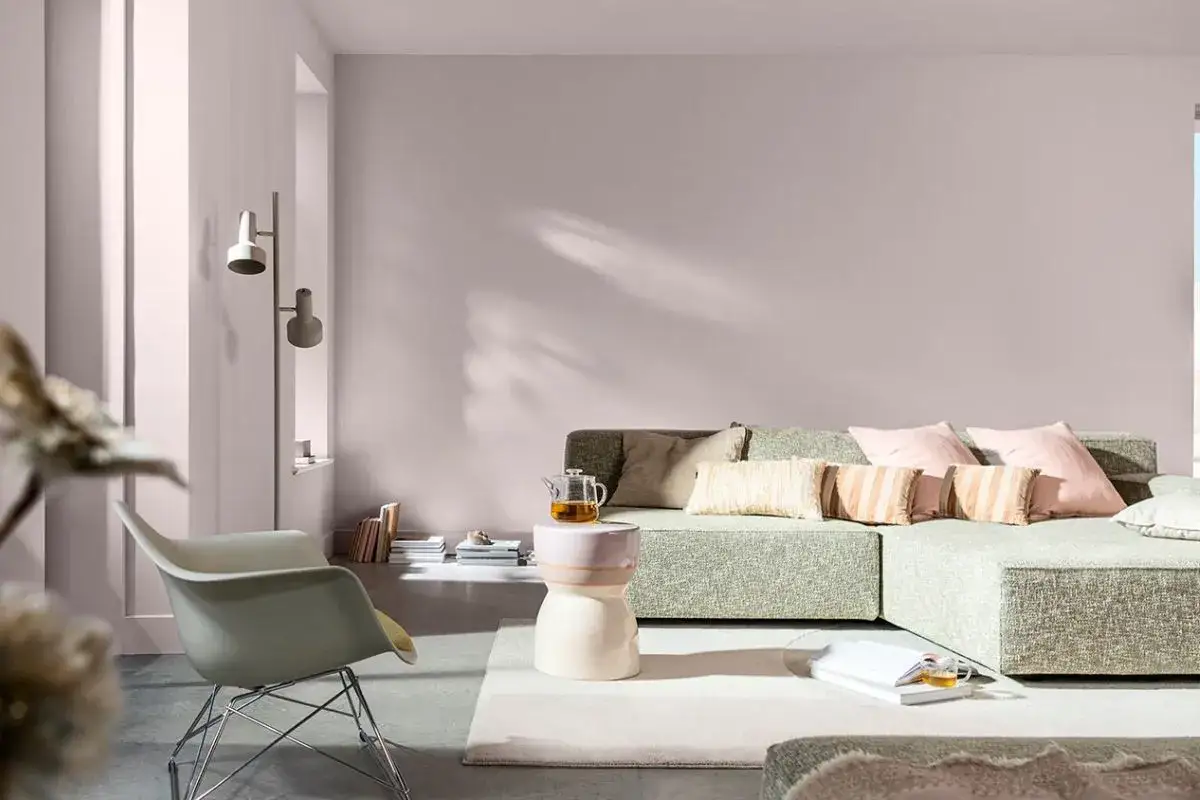 Salotto con divano modulare verde, poltrona chiara e tavolino. Le pareti rosa cipria e i cuscini rosa e beige evocano **colori primaverili**.